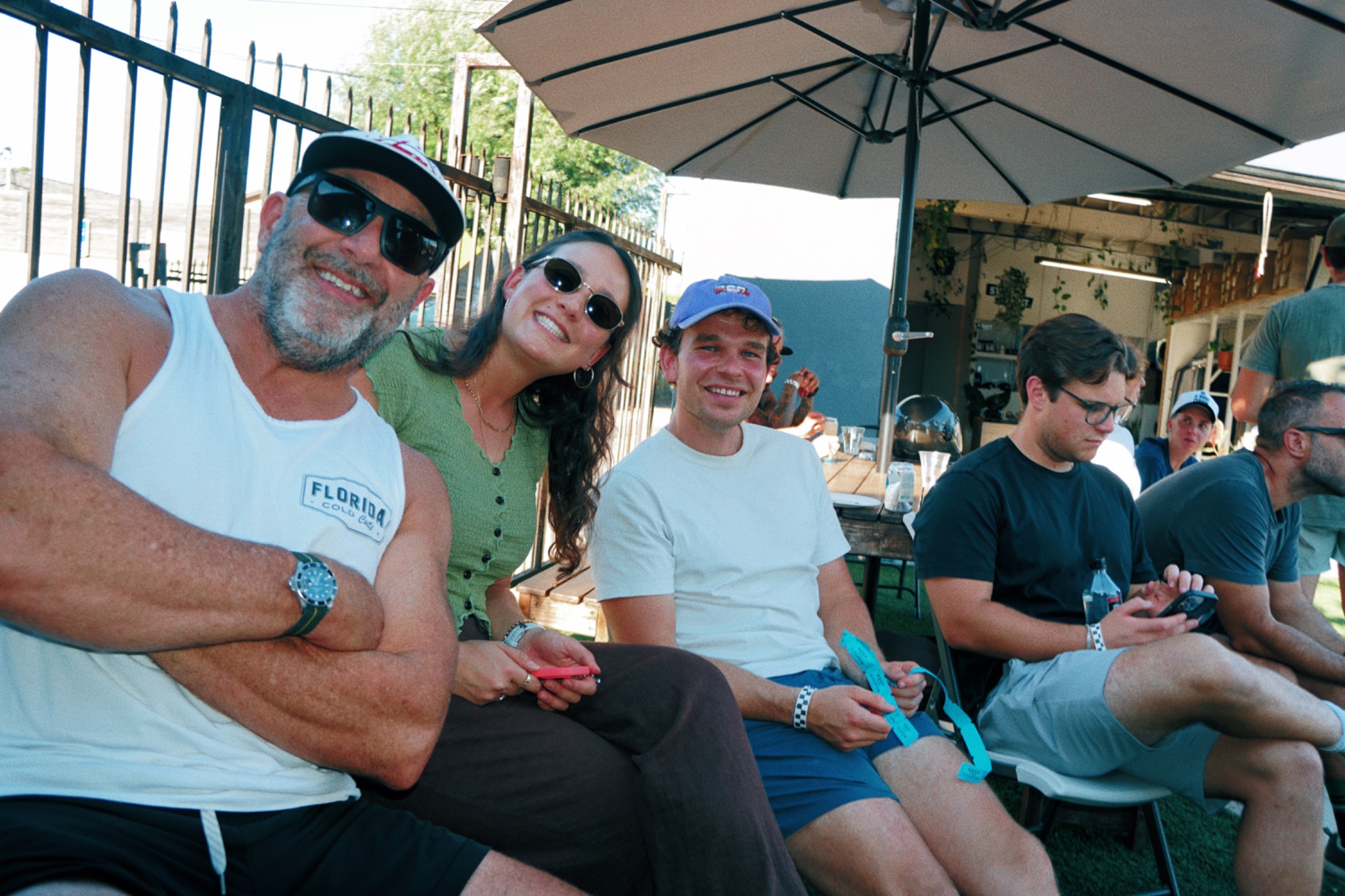 Smiling DEUCE Gym community members gathered around a patio table under an umbrella