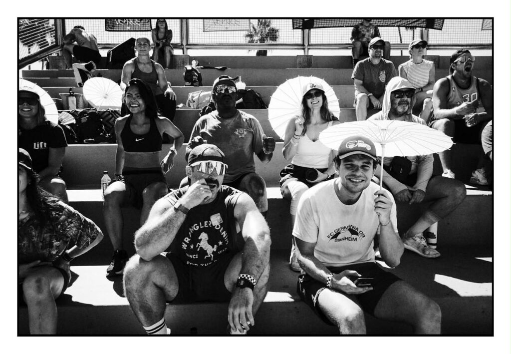Black and white photo of a smiling crowd of DEUCE Gym members sitting together in the stands