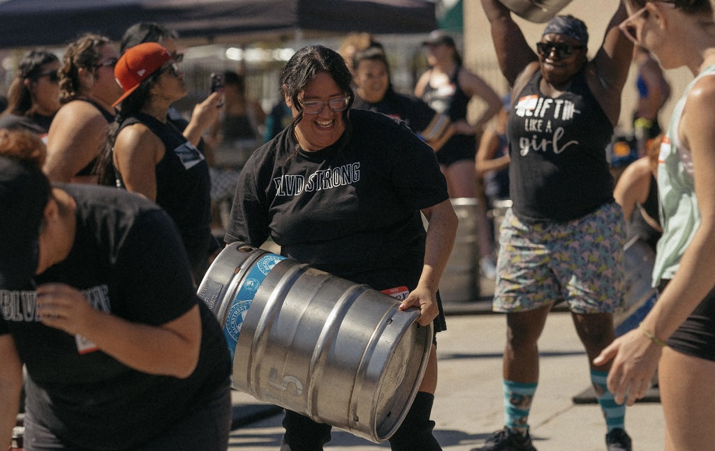 Women lifting and carrying a strongman keg together at a DEUCE Gym strongman event