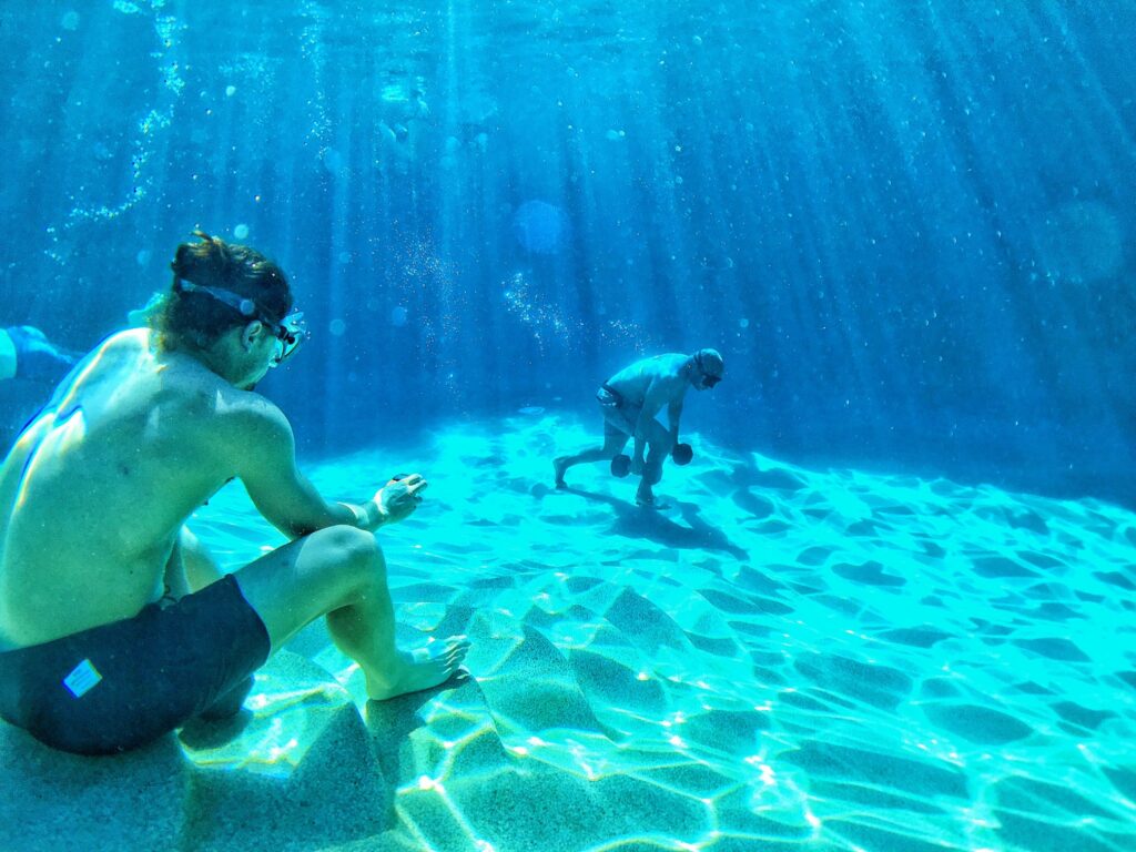 Two athletes doing underwater dumbbell training on the bottom of a clear blue pool